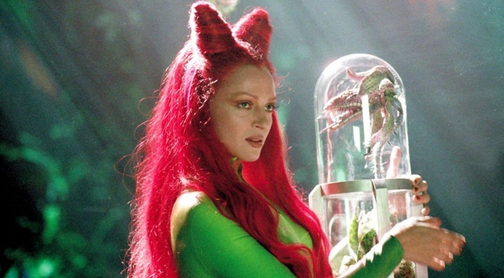 Uma Thurman als Poison Ivy. In den Armen umschlingt sie ein großes Laborglas, in dem eine Pflanze ist, die aussieht, als könnte sie fleischfressend sein. (Bild: Warner Bros.)