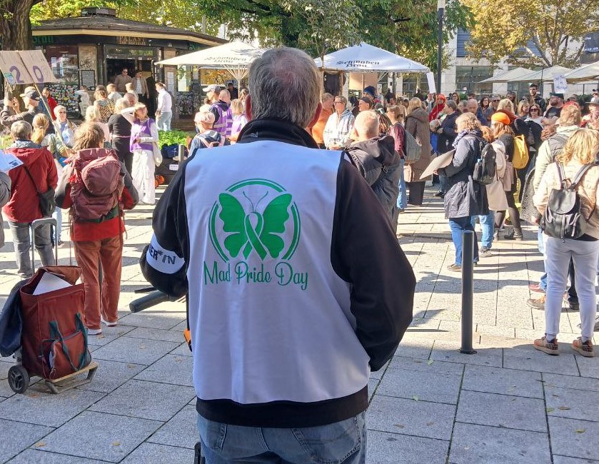 Ein Ordner in weißer Weste beim Stuttgarter Mad Pride Day 2025, von hinten zu sehen. Vor ihm Demonstrierende.