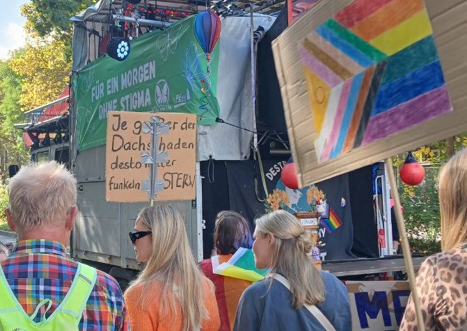 Teilnehmer*innen der Stuttgarter Mad Pride Parade 2025. Sie tragen Demoschilder, im Hintergrund der Musikwagen.