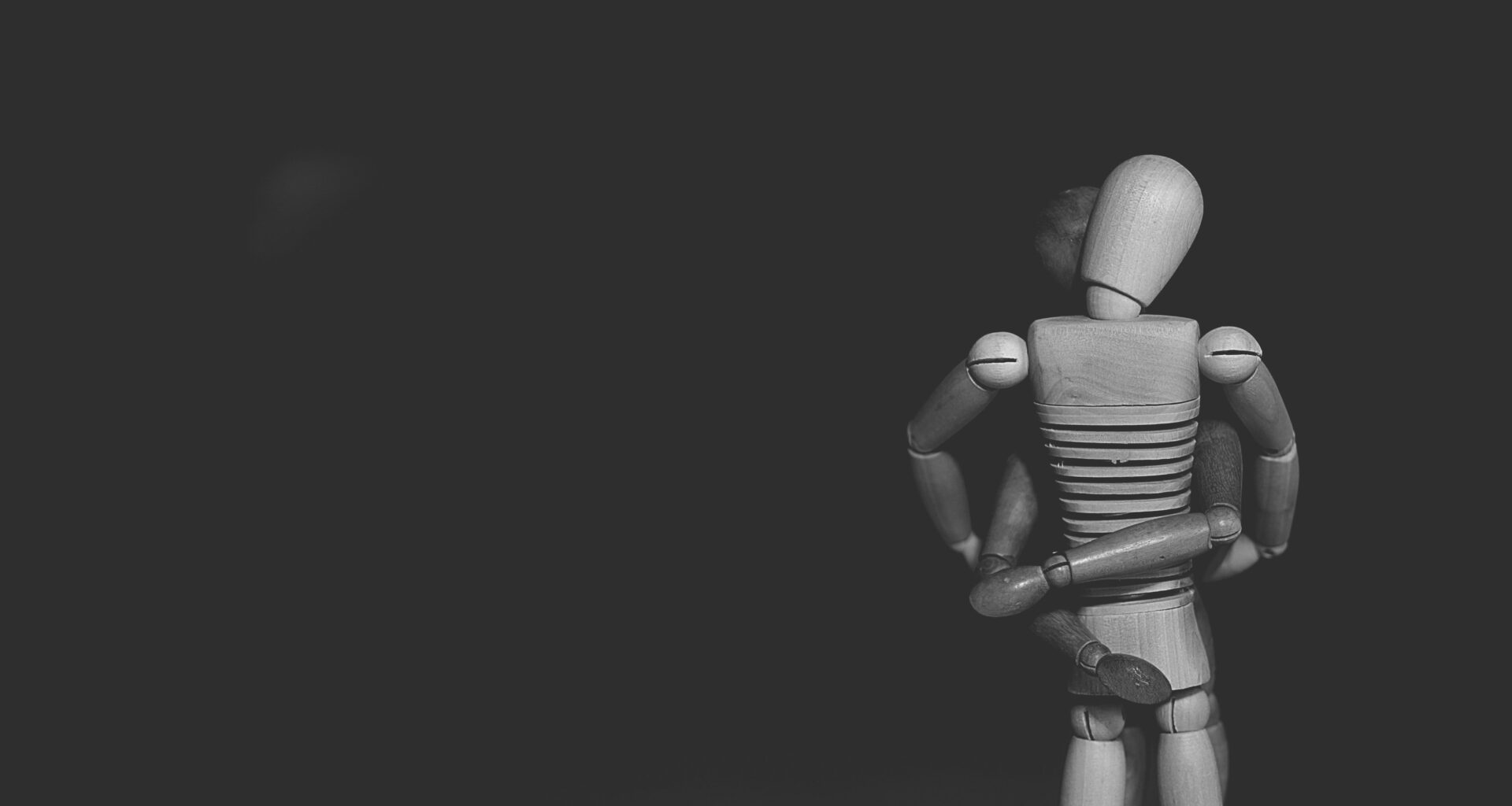 Vor schwarzem Hintergrund umschlingen sich zwei Holzpuppen, die Schaufensterfiguren ähneln. (Foto: Gaelle Marcel auf Unsplash)