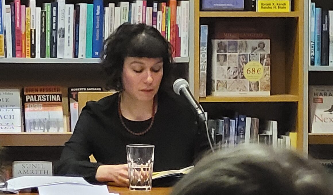In dunkler Kleidung sitzt Sarah Lorenz vor einem Bücherregal in der Freiburger Buchhandlung Schwarz und liest aus ihrem Roman „Mit dir, da möchte ich im Himmel Kaffee trinken“ vor. (Foto: vliestext)