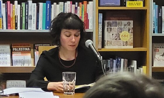 In dunkler Kleidung sitzt Sarah Lorenz vor einem Bücherregal in der Freiburger Buchhandlung Schwarz und liest aus ihrem Roman „Mit dir, da möchte ich im Himmel Kaffee trinken“ vor. (Foto: vliestext)