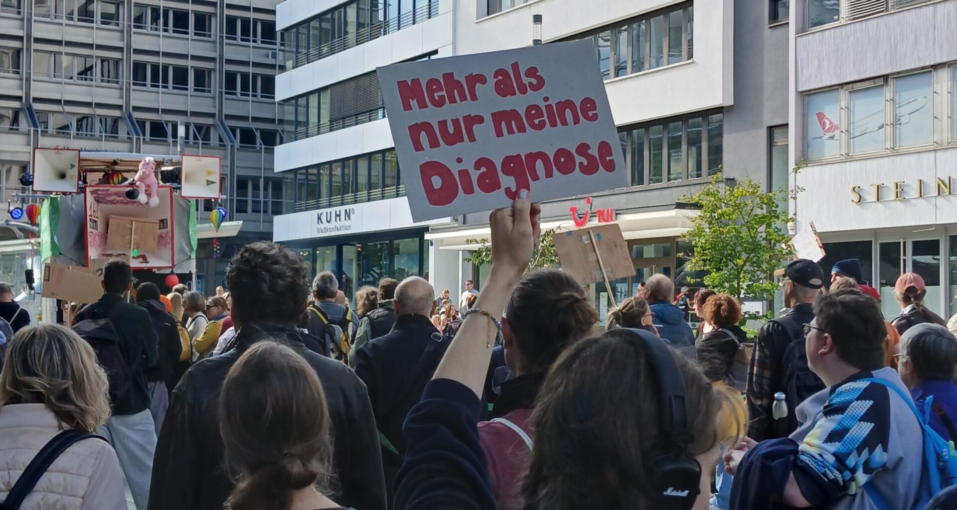 Mad-Pride-Demo in Stuttgart 2025. Jemand hält eine Schild hoch, auf dem in roter Schrift steht: Mehr als meine Diagnose. (Foto: vliestext)
