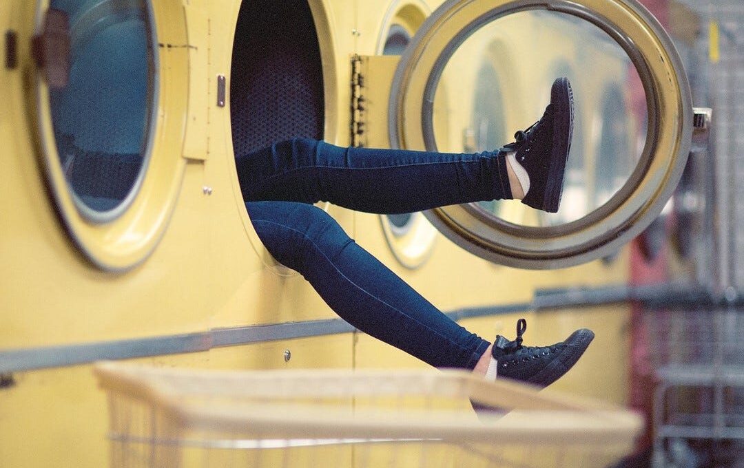 In einem Waschsalon schauen die Beine einer Person aus einer Waschmaschine heraus. (Bild: Pexels auf Pixabay)