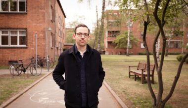 Titelbild: In dunkler Kleidung steht Paul Bokowski, der Autor von „Schlesenburg“, vor Häusern im Innern der Berliner Schillerpark-Siedlung und schaut in die Kamera.