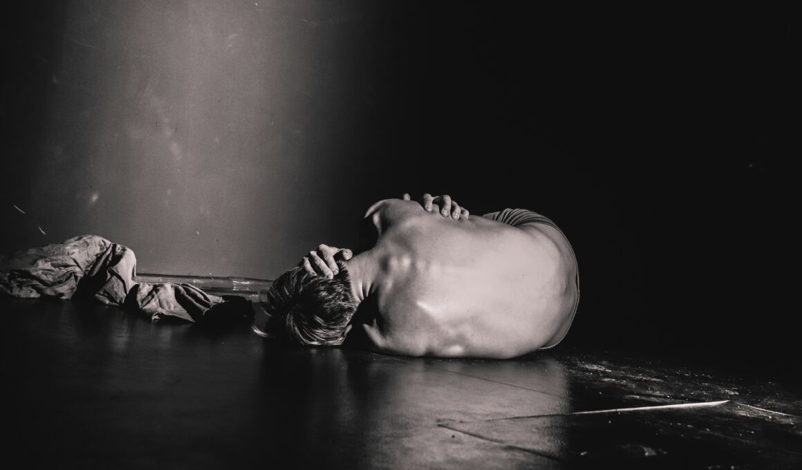 Graustufenbild: Mensch liegt halbnackt in verzweifelter Embryonalhaltung auf einem dunklen Boden. Zu sehen ist vor allem der Rücken.